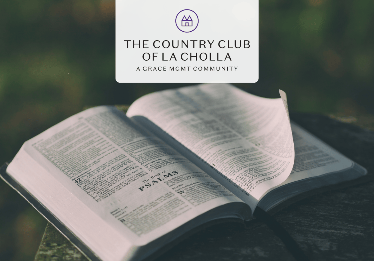 Open Bible on a wooden surface outdoors with a white rounded card displaying The Country Club of La Cholla logo on top.