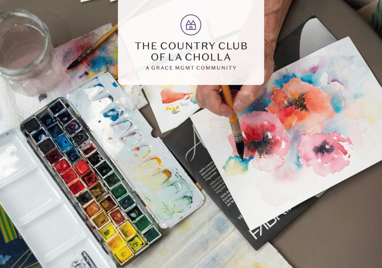 Artist's workspace with watercolor paints and a hand painting bright pink and orange flowers; logo overlay for The Country Club of La Cholla.